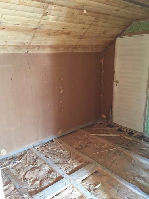 Inre hörn av ett rum under renovering med oskyddad isolering och brun gipsskiva på väggen.