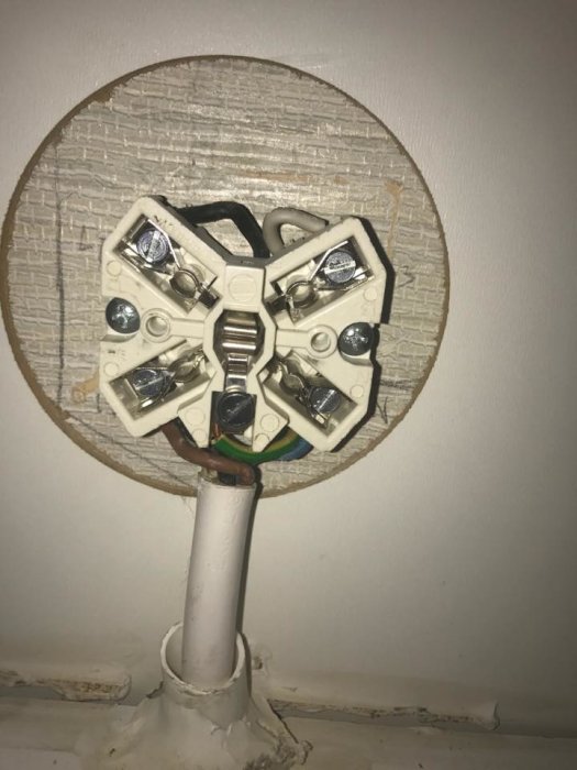 Öppen spiskontakt med oskyddade kablar och terminaler mot en vägg med textur.