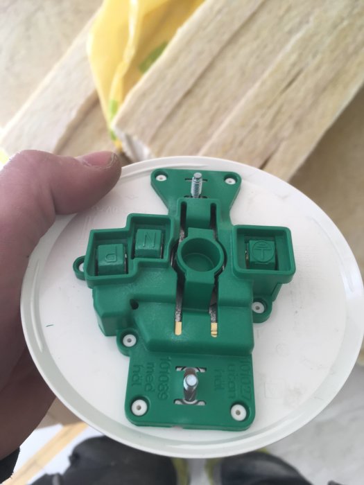 Hand håller en grön takdosa utan lock med synliga anslutningar, avsedd för installation i tak.