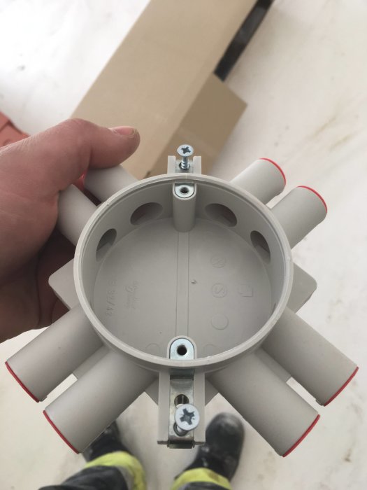 Hand håller en modern takdosa med flera röranslutningar och fästskruv, utan gänga för centrumskruv.