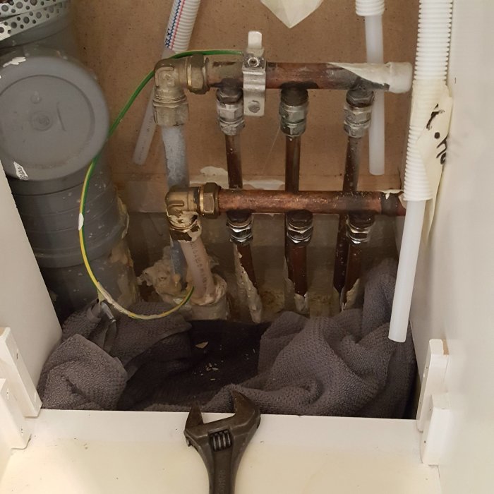 VVS-installation med pex-rör anslutna till kopparrörsfördelare och en skiftnyckel i ett badrum.