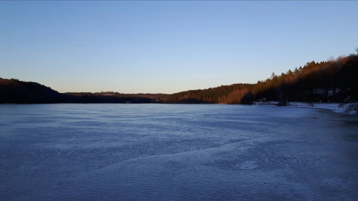 Istäckt Fixsjön omgiven av skog under sen eftermiddag med spår av promenad på isen.