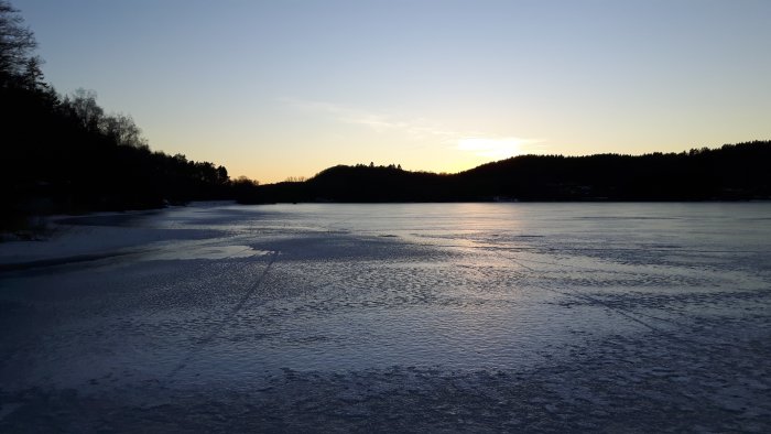 Solnedgång över en istäckt Fixsjö med spår på isen och skog i bakgrunden under senvintern.