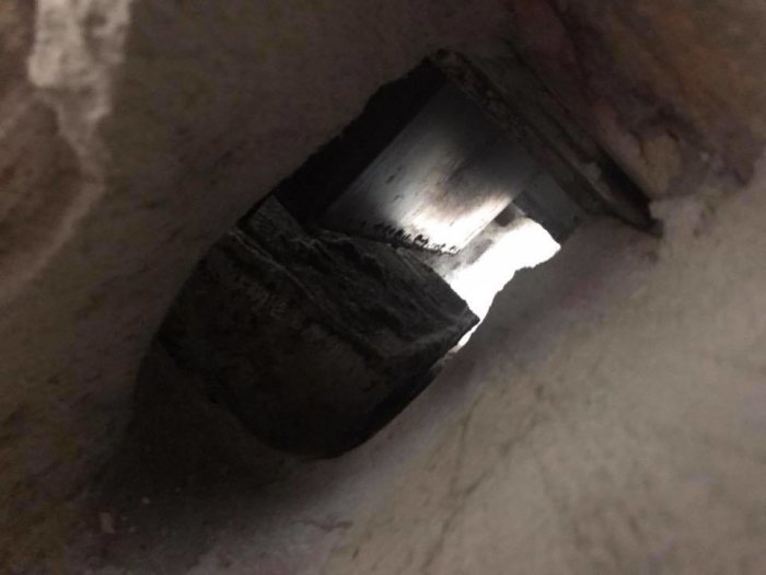 Mörk bild på en äldre murstockventil, smutsig och delvis upplyst, i samband med en renoveringsfråga.