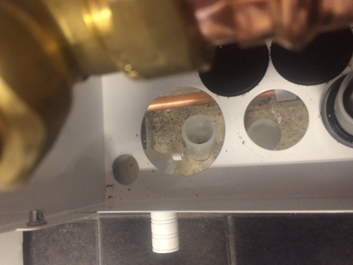 Insyn i skåp med urplockade tätningspluggar och synliga rör genom hål med diametrar 65 och 40 mm.