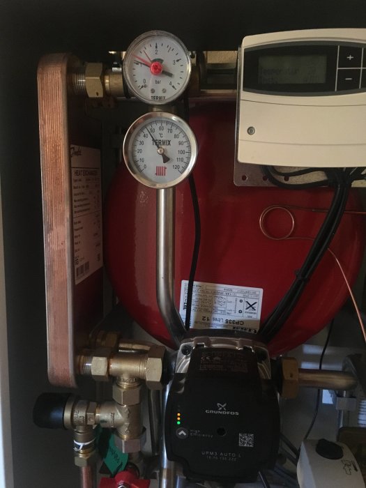Värmesystem med tryckmätare, temperaturregulator och pump i ett pannrum.