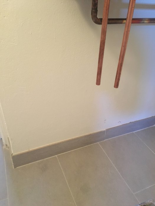 Kopparledningar längs en vägg med fuktspår vid golvlisten.
