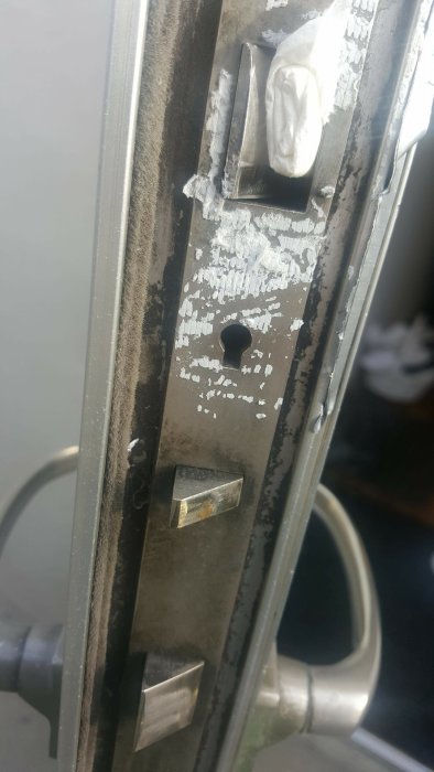 Närbild på ett gammalt lås med skadad yta och en nyckelhålstäckning i metall.