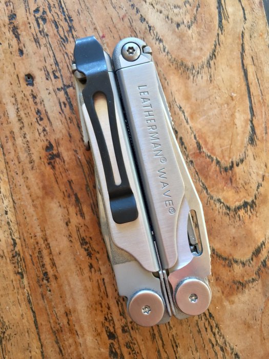 Folded Leatherman Wave multiverktyg med sidoklipp på ett slitet träbord.