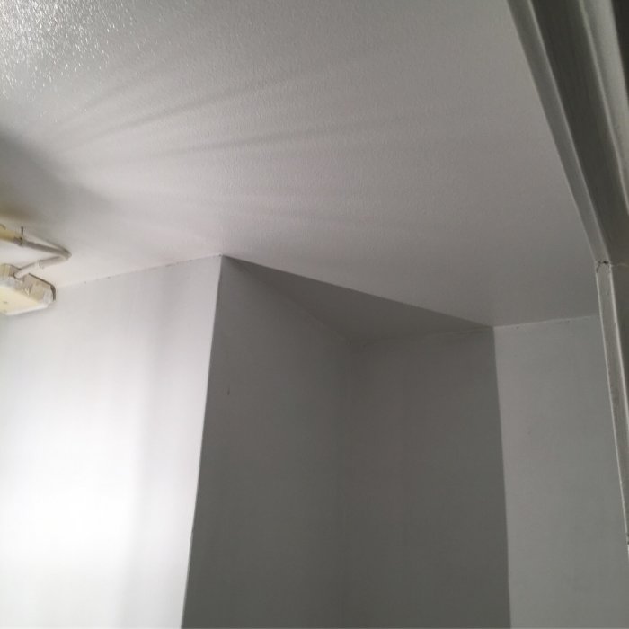Nyrenoverade vita väggar och tak i ett rum med synlig taklampa och skuggspel.