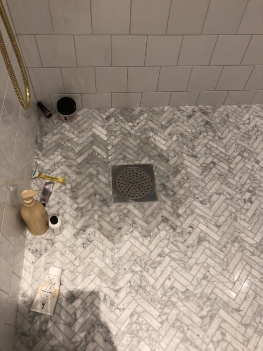 Nylagd klinkers i badrum med mörkare område runt golvbrunnen, uppställda rengöringsmedel.