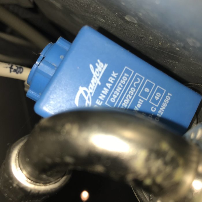 Närbild på en blå magnetventil av märket Danfoss, med märkningar och rörkopplingar synliga.