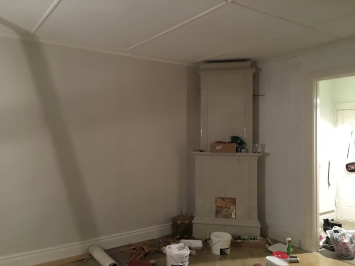 Ny tapet på vänstra väggen bredvid vit kakelugn i ett rum under renovering.