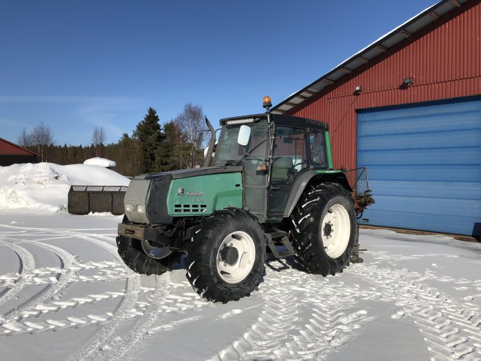 Valmet 6400 traktor i snö utanför en röd lada med blå port, tydliga spår av salt på fordonet.