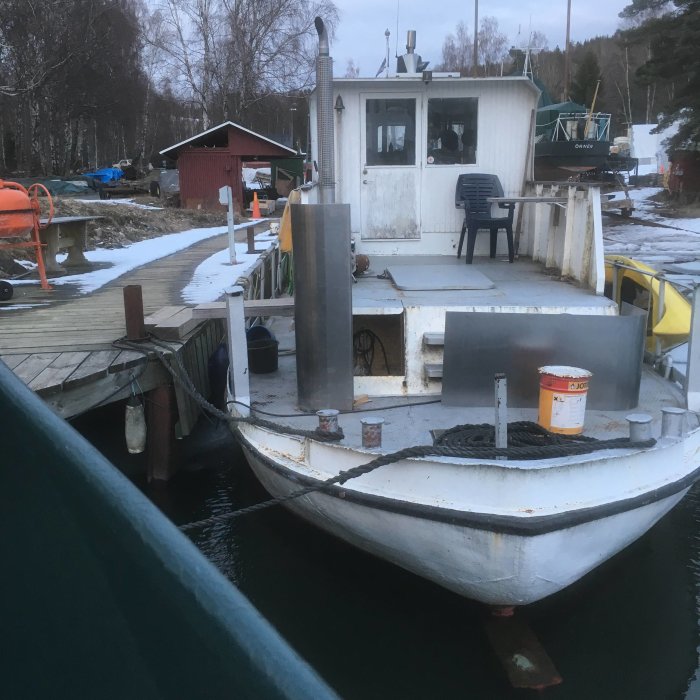 En båt förtöjd vid en brygga med byggnader och byggmaterial i bakgrunden.