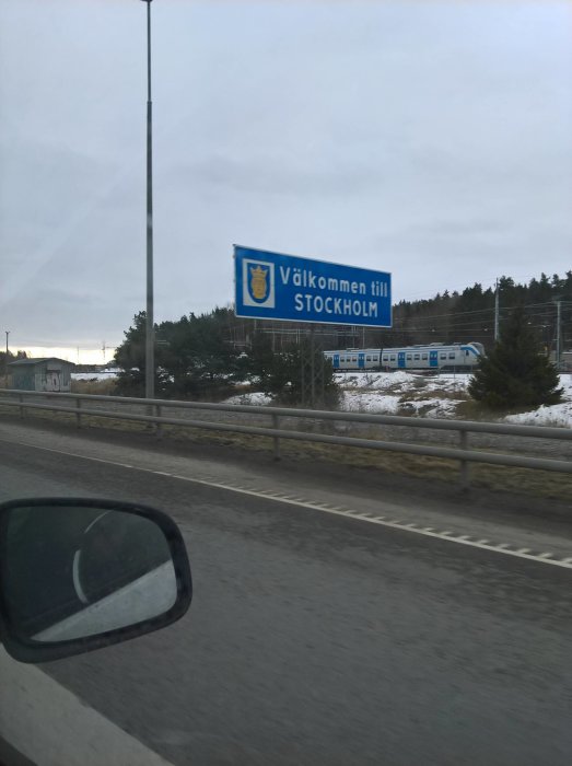 Skylt med texten "Välkommen till STOCKHOLM" sedd från ett fordon på en molnig dag.