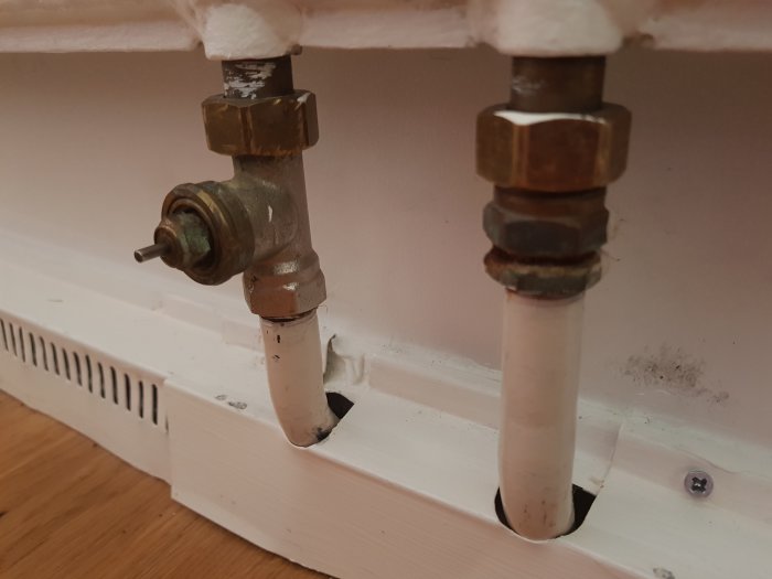 Närbild av ett radiatorrör och en sexkantskruv vid en elementanslutning mot en vägg.