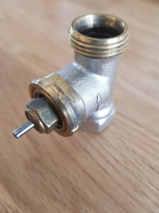 Metallförgrening med en framträdande sexkantsskruv på träbakgrund.