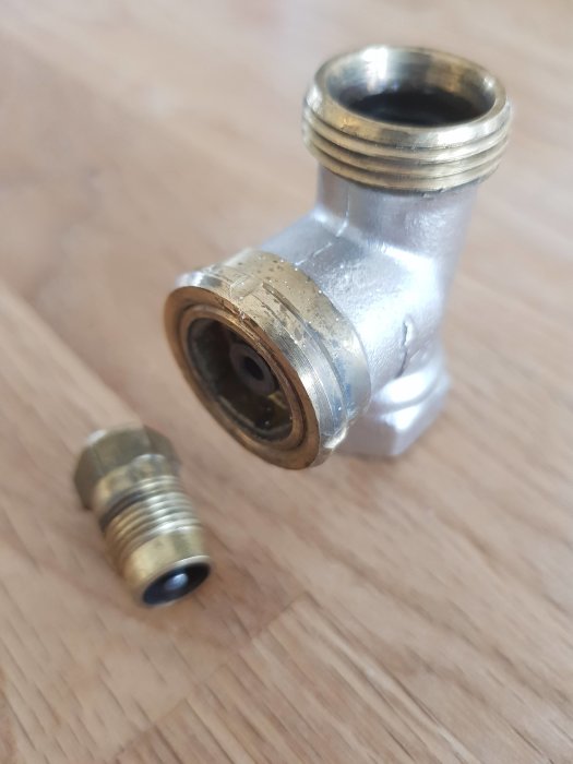 Vinkelrör med sexkantskruv och O-ring vid sidan på ett träunderlag.