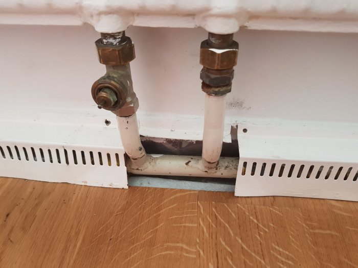 Rör från borttaget element med bypass och rörkopplingar synliga bakom golvlisten.