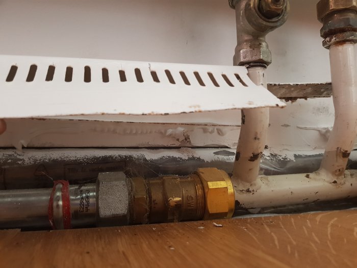 Radiator med synliga rörkopplingar, varav en är nyare, under en vitmålad fönsterbräda.