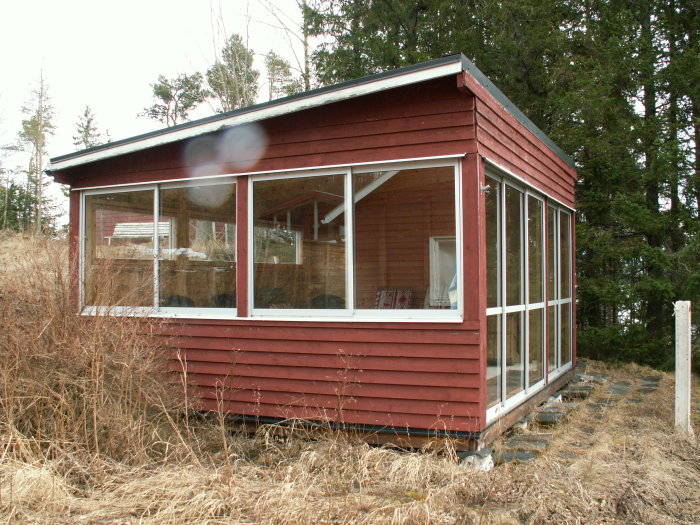 Fristående inglasad uteplats till fritidshus med röda träväggar och stora fönsterpartier.