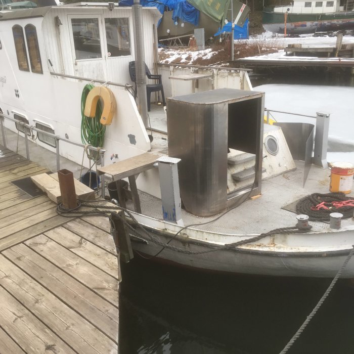 Delar av ett renoveringsprojekt på en båt belägen vid en brygga, med snötäckt mark i bakgrunden.
