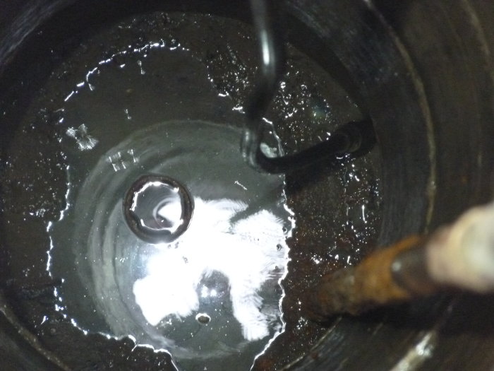 Vy inuti en brunn med vatten och löst hängande PEM-rör ovanför botten, gammalt järnrör synligt.