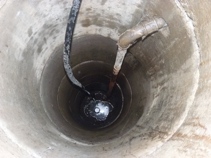 Vy inuti en brunn med ett löst hängande PEM-rör och ett gamalt järnrör som sträcker sig in i vattnet.