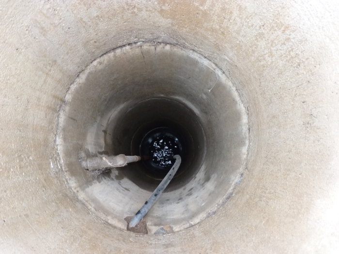 Inuti en brunnskonstruktion med löst hängande PEM-rör och synligt äldre järnrör som sticker upp.