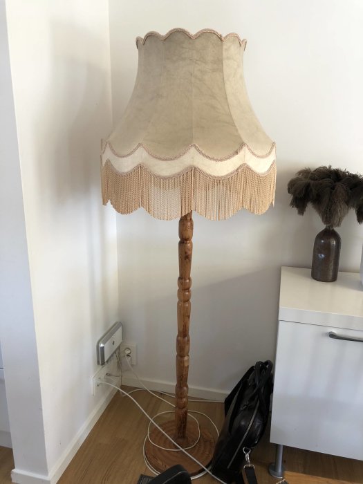 Golvlampa med stor, textilerad lampskärm i vintagestil stående i ett hörn av ett rum.