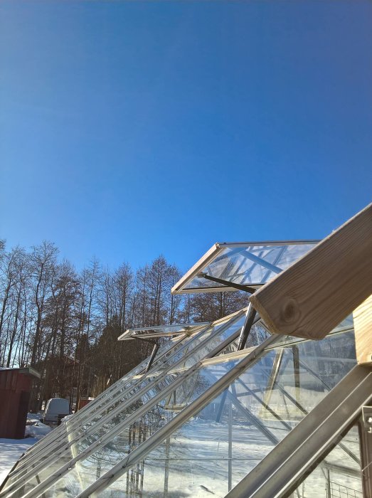 Automatiskt öppnade luckor på ett rad av växthus mot en klarblå himmel, med snötäckt mark i bakgrunden.