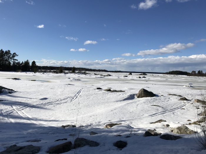 Snötäckt landskap med spår och isformationer under blå himmel.