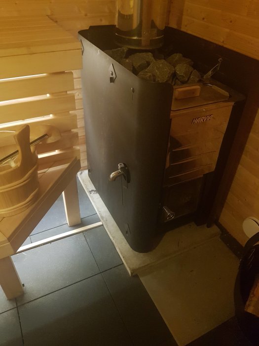 En Harvia 20 ES PRO kamin i ett sauna, med synliga stenar och märkesnamn på trälådan.