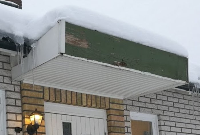 Entrétak till ett hus skadat av storm, med synliga trädelar och täckt av snö.