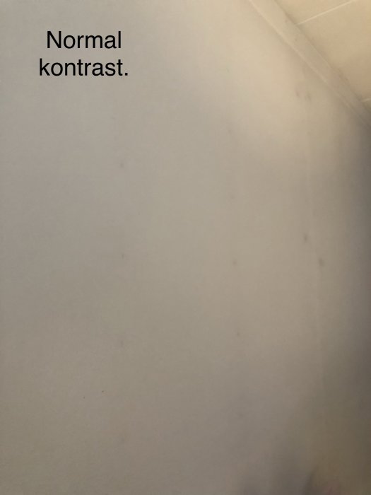 Vit vägg med synliga gipsspikar och utbuktningar, text "Normal kontrast" i övre delen.