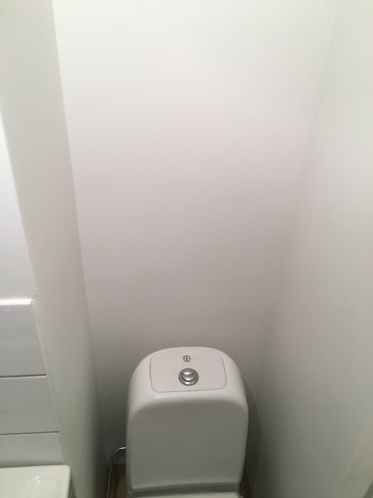 Nymålade vita väggar i ett hörn över en toalettstol, bild med låg kvalitet.