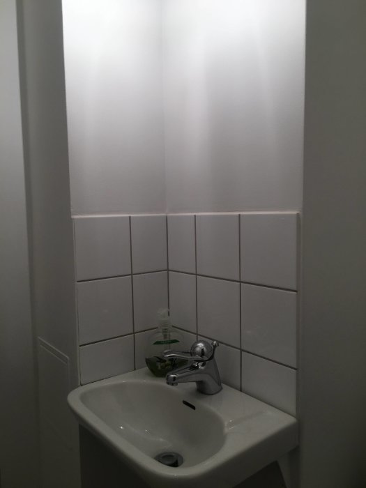Nymålad vägg ovanför handfat med vita kakelplattor i ett badrum.