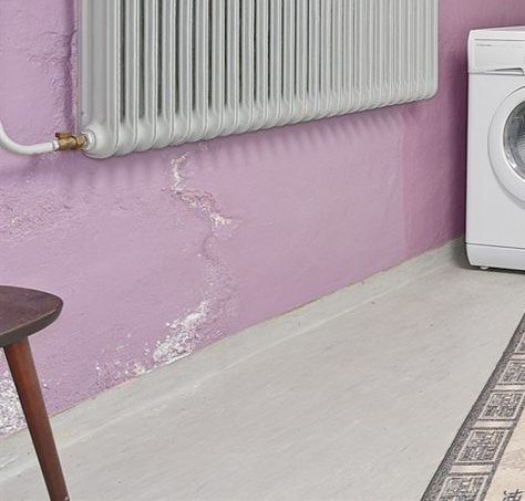 Källarvägg med en synlig lagad spricka intill en tvättmaskin och en radiator, utan fuktfläckar eller missfärgningar.