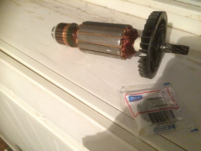Elmotoraxel med pinjongdrev bredvid nytt kullager i förpackning.