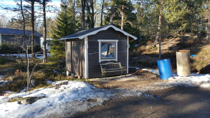 En friggebod omgiven av snö och barrträd i solljus.