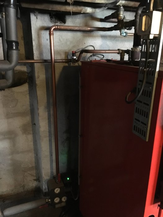 Installationsvy av en laddomat utan isolering bredvid en röd panna i ett verktygsrum.
