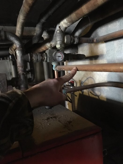 Person pekar på ett tryckmätare kopplat till VVS-system ovanför en röd panna.