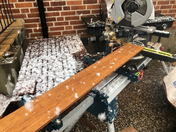 Sågstation utomhus med ett mörkfärgat bambugolvplank på sågbordet, täckt av snöflingor.