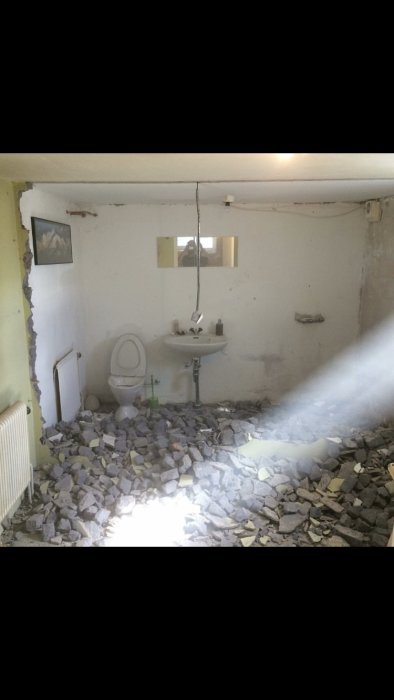 Renoverad källare med riven mellanvägg, toalett och handfat omgivna av gråsten och byggavfall.