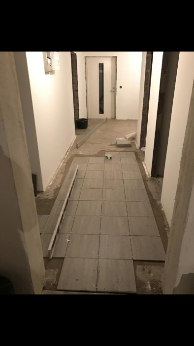 Renoveringsprocess av hall med nyinstallerade 30x30 granitkeramikplattor och ett synligt arbetsområde.