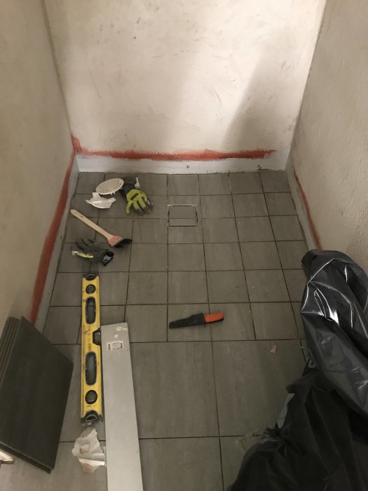 Installation av klinkergolv med verktyg och nivelleringsutrustning i en halvfärdig badrumsrenovering.