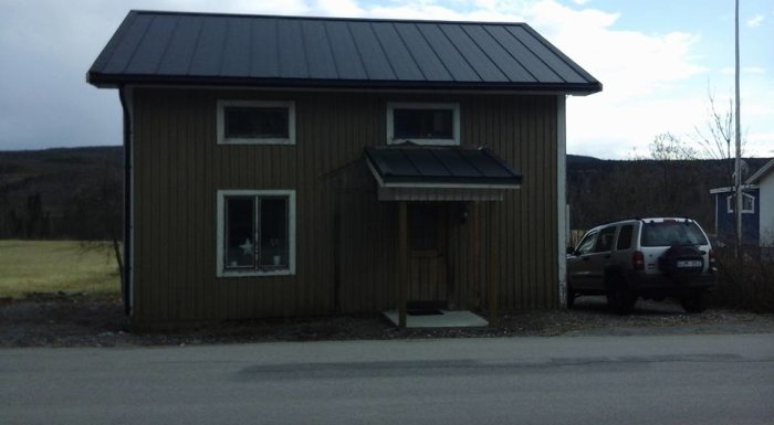 Tvåvånings trähus med sadeltak vid landsväg, bil parkerad till höger.