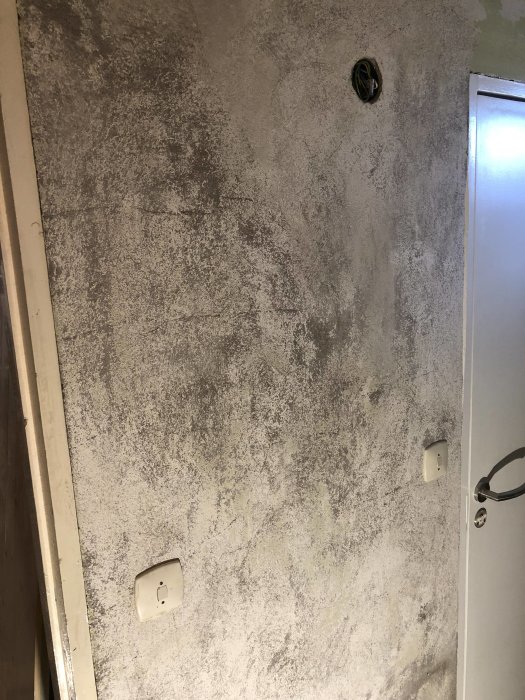 Källarvägg med bortskrapade gröna färglager som visar underliggande kritig vit yta.