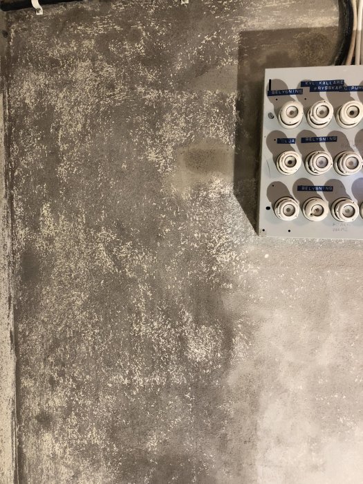 En delvis avskrapad källarvägg med rester av grön plastfärg och en strömbrytartavla.
